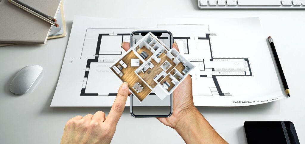Hand holding smartphone displaying 3D house model over architectural floor plan on desk